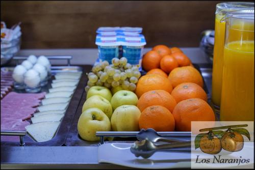a table with apples oranges and other fruits and juice at Hostal y Apartamento Rural Los Naranjos in Melegis
