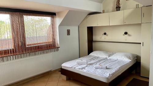 a bedroom with a bed with white sheets and two windows at Gyula Vár Panoráma Apartman in Gyula