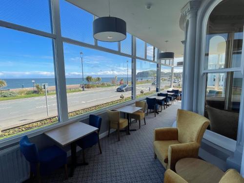 スランディドノにあるHydro Hotelのテーブルと椅子が備わり、海の景色を望むレストラン
