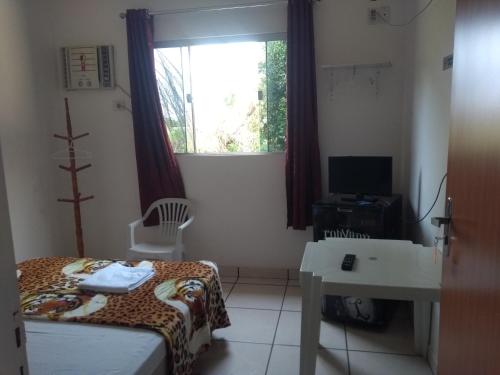 a bedroom with a bed and a desk and a window at Chácara Pousada Sagui in Cuiabá