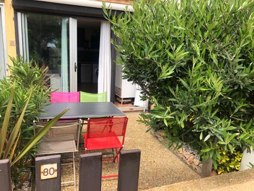 une table noire avec des chaises colorées dans un jardin dans l'établissement Studio cabine GRUISSAN PLAGE DU GRAZEL, à Gruissan