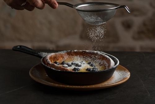 a person is sprinkling powdered sugar on a bowl of food at MiraMe Athens Boutique Hotel in Athens