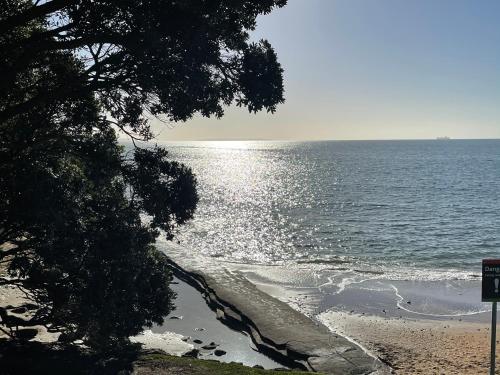 a view of a beach with the sun reflecting on the water at Whitby Studio - Mairangi Bay Beach in Auckland