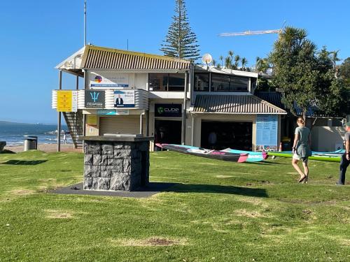 a couple of people walking around a building with surfboards at Whitby Studio - Mairangi Bay Beach in Auckland