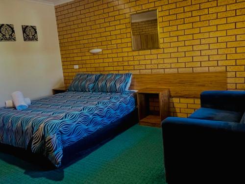a bedroom with a bed and a chair and a brick wall at Lake Mulwala Hotel in Mulwala