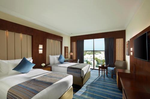 a hotel room with two beds and a television at Royal Tulip Muscat in Muscat