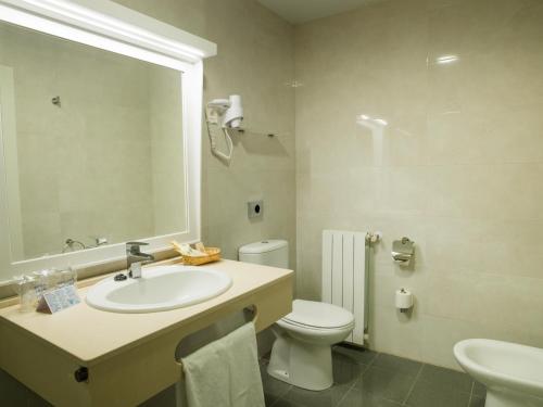 Un baño con lavabo, inodoro y espejo. en Hotel Monarque Torreblanca, en Fuengirola