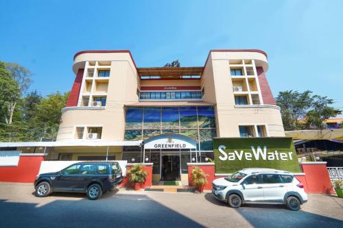 two cars parked in a parking lot in front of a building at Hotel Green Field in Satara