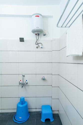 a white tiled bathroom with a light and blue stool at Hotel Green Field in Satara