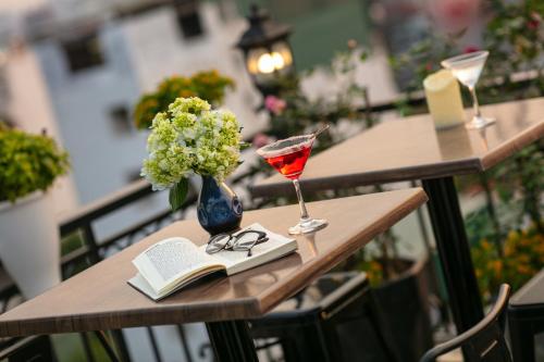 a table with a book and a glass of wine and a vase of flowers at Carillon Boutique Hotel in Hanoi