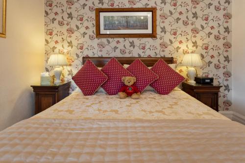 a teddy bear sitting on a bed with red pillows at Beechwood in Bowness-on-Windermere