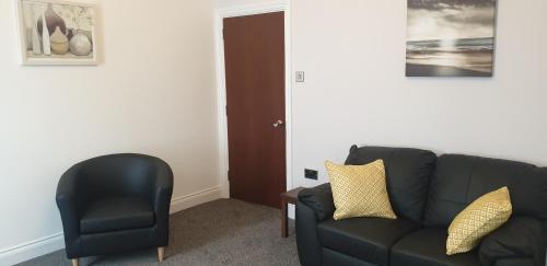 a living room with a black couch and a chair at Glentworth Holiday Apartments in Tenby