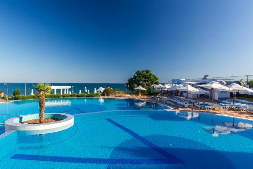 a large swimming pool with a palm tree next to the ocean at Sineva Beach Hotel - All Inclusive in Sveti Vlas