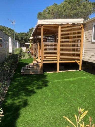 a backyard with a wooden pergola and green grass at Bungalow in Canet-en-Roussillon