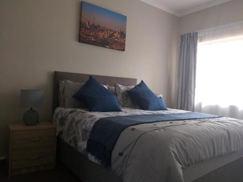 a bedroom with a bed with blue pillows and a window at Burban Bliss in Johannesburg