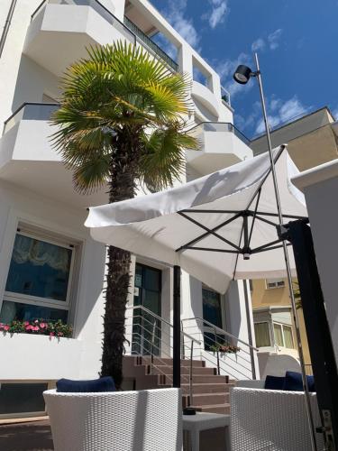 ein weißes Haus mit einer Palme, Stühlen und einem Regenschirm in der Unterkunft Residence Aida in Rimini