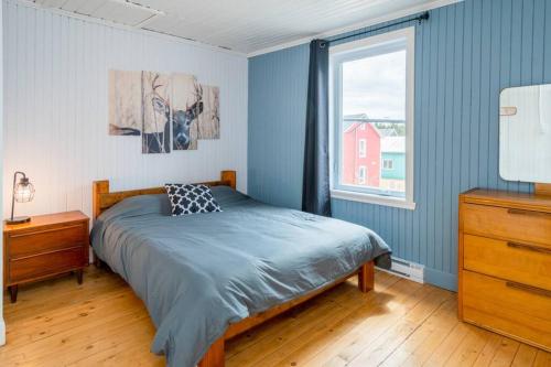Dormitorio azul con cama y ventana en Refuge du Massif - Halte au cœur du village, en Saint-Philémon