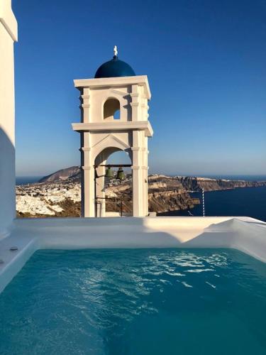 a swimming pool with a clock tower in the background at Altana Heritage Suites in Imerovigli