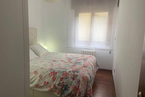 Un dormitorio con una cama con una manta de flores y una ventana en Apartamento en el Paseo de Manuel Noriega, Nº 9, con jardín privado, Wifi, en Comillas, en Comillas
