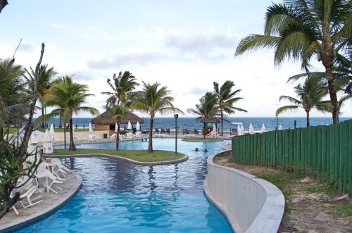 a resort swimming pool with palm trees and the ocean at Bangalô Luxo Beach Class Resort Muro Alto in Porto De Galinhas
