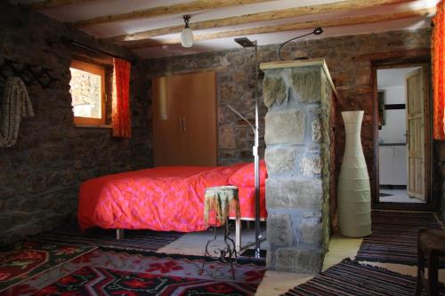 een slaapkamer met een rood bed en een stenen muur bij Guest House Ktona in Dardhë
