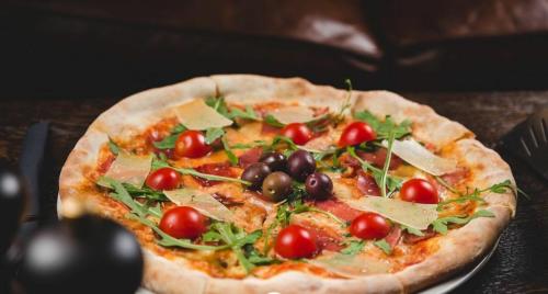 a pizza with tomatoes and olives on a table at Hotel Keto in Podgorica