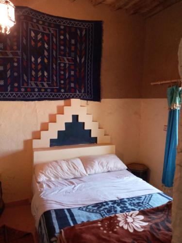 a bed in a room with a tapestry on the wall at Family Moroccan House in Merzouga