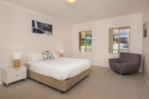 a white bedroom with a bed and a chair at Seachange in Dunsborough