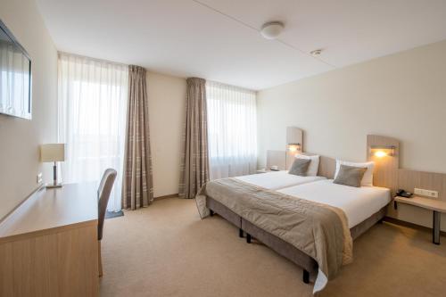 a hotel room with a large bed and a desk at Fletcher Wellness-Hotel Kamperduinen in Kamperland