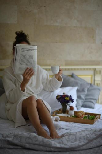 Vintage na Bulvare في أوديسا: امرأة مستلقية في السرير تقرأ كتاب وتمسك بفنجان