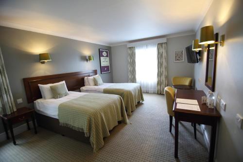 a hotel room with two beds and a desk at Mercure Gloucester Bowden Hall Hotel in Gloucester
