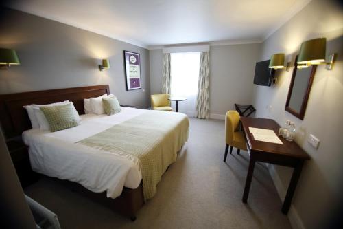 a hotel room with a large bed and a desk at Mercure Gloucester Bowden Hall Hotel in Gloucester
