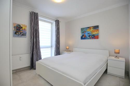 a white bedroom with a white bed and a window at Dünenblick Wohnung 27 in Boltenhagen