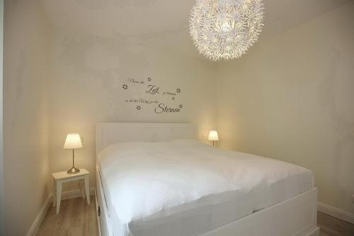 a bedroom with a white bed and a chandelier at Strandvilla Scholle - Lachs Wohnung 01 in Boltenhagen