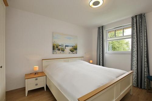 a white bedroom with a large bed and a window at Reethaus Am Mariannenweg 12a in Boltenhagen