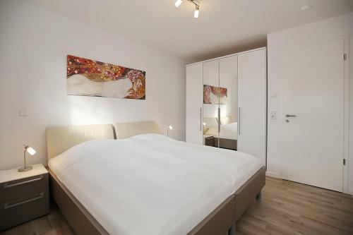 a white bedroom with a large bed and a mirror at Reethaus Am Mariannenweg 06b in Boltenhagen