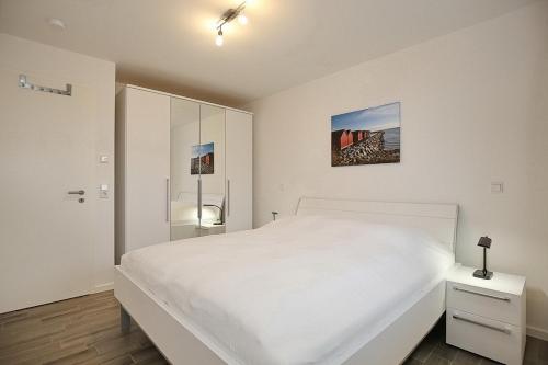 ein weißes Schlafzimmer mit einem weißen Bett und einem Schrank in der Unterkunft Reethaus Am Mariannenweg 06a in Boltenhagen