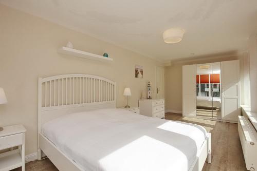 Dormitorio blanco con cama blanca y espejo en Strandvilla Krabbe Wohnung 04, en Boltenhagen