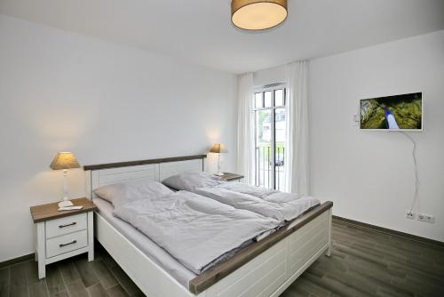 a white bedroom with a large bed and a window at Linden-Palais Wohnung 14 in Heiligendamm