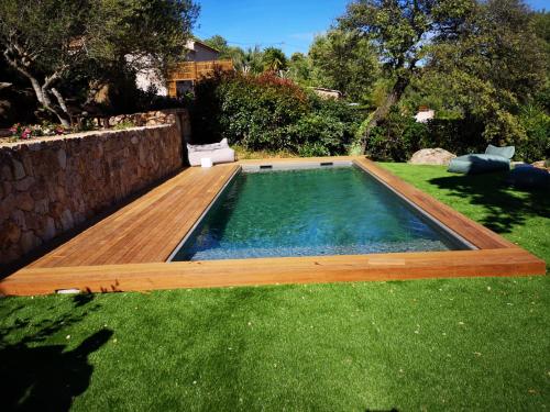 a swimming pool with a wooden deck in the grass at Bel appartement dans hameau calme in Bonifacio