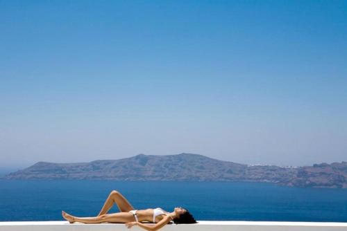 a woman laying on the beach with the ocean in the background at Xenones Filotera in Imerovigli