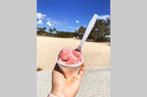 a hand holding a cup of pink ice cream with a spoon at Serenity at Seascape: Steps to the beach & Shops in Palm Beach Shores