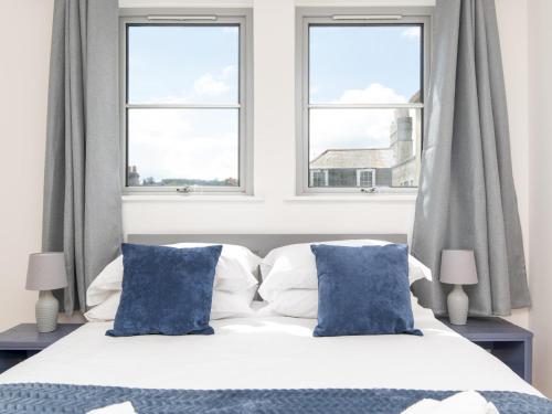 uma cama branca com almofadas azuis e 2 janelas em Pass the Keys Bright modern one bed apartment - Bath city centre em Bath