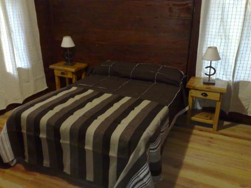 a bed with a black and white striped blanket and two tables at Estancia Laguna Vitel in Chascomús