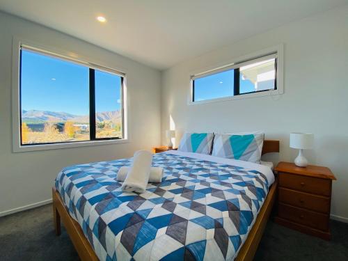a bedroom with a bed with a checkered blanket and two windows at Flat White in Lake Tekapo