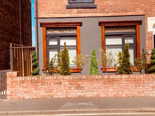 a house with a brick wall with potted trees at Charming Spacious Apartment, Kidderminster in Kidderminster