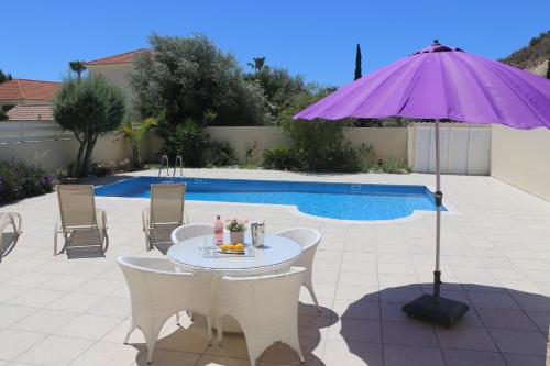 einen Tisch mit einem lila Sonnenschirm neben einem Pool in der Unterkunft Villa Rossa in Pissouri