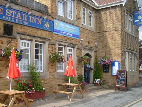 un hombre parado fuera de un edificio de ladrillo con dos sombrillas en The Star Inn, en Nafferton