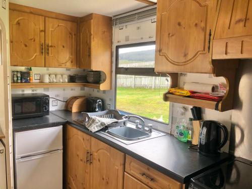 uma cozinha com armários de madeira, um lavatório e uma janela em Lettoch Farm Holiday Home em Dufftown
