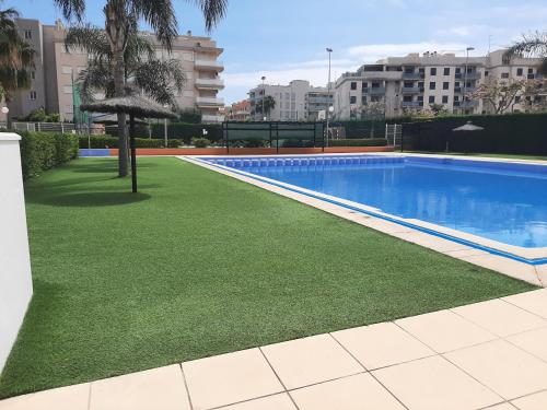 een zwembad met groen gras naast een gebouw bij Apartamento playa canet d'en Berenguer in Canet de Berenguer
